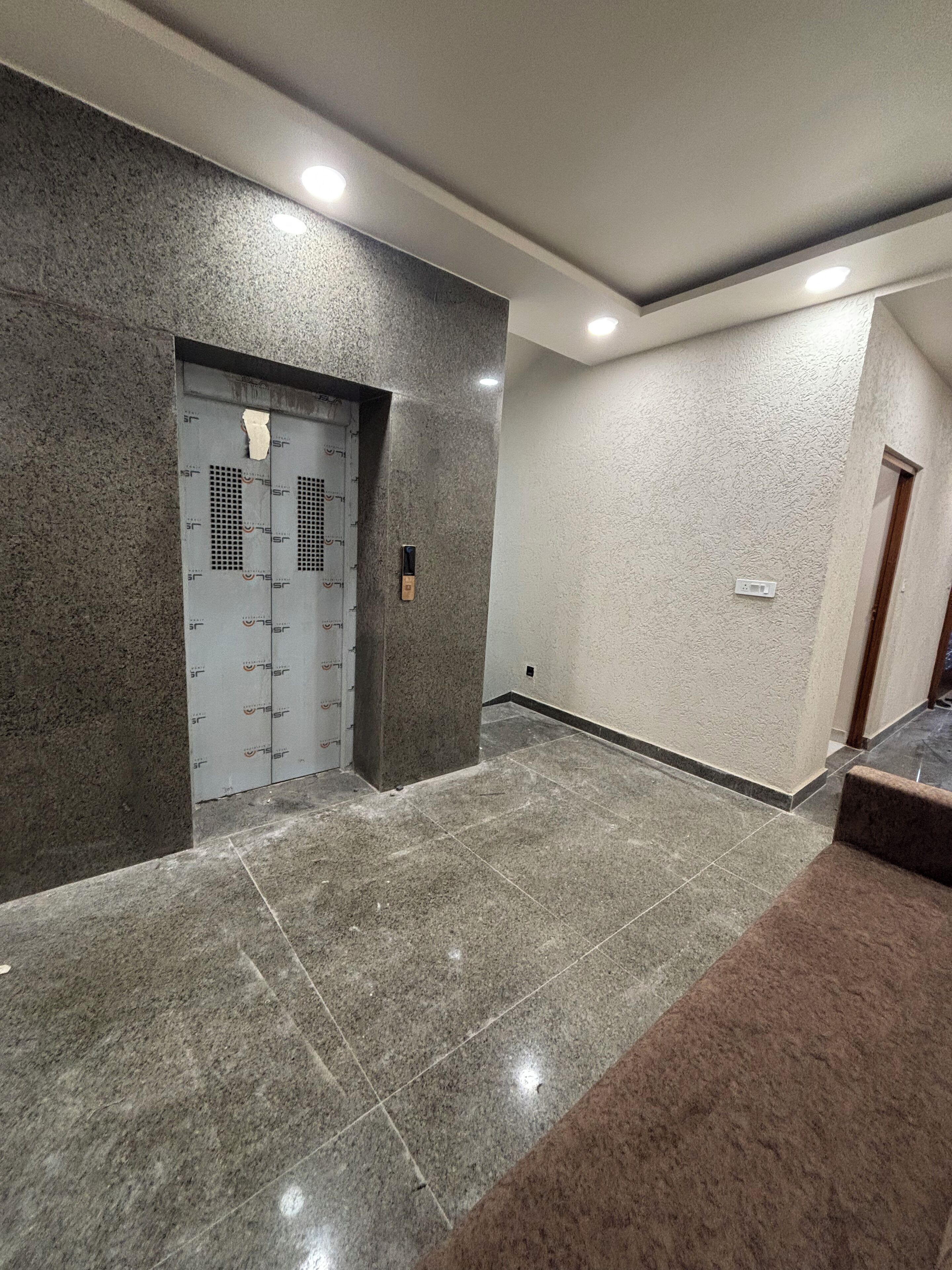 A modern hallway with a grey tiled floor, a grey textured wall, and a door with a security keypad.