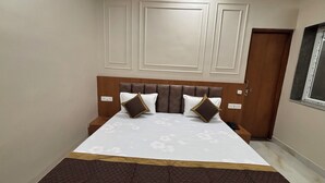 A neatly made bed with a headboard, a bedside table, and a wall-mounted light fixture. - Hotel Kajal Inn (Ajmer)
