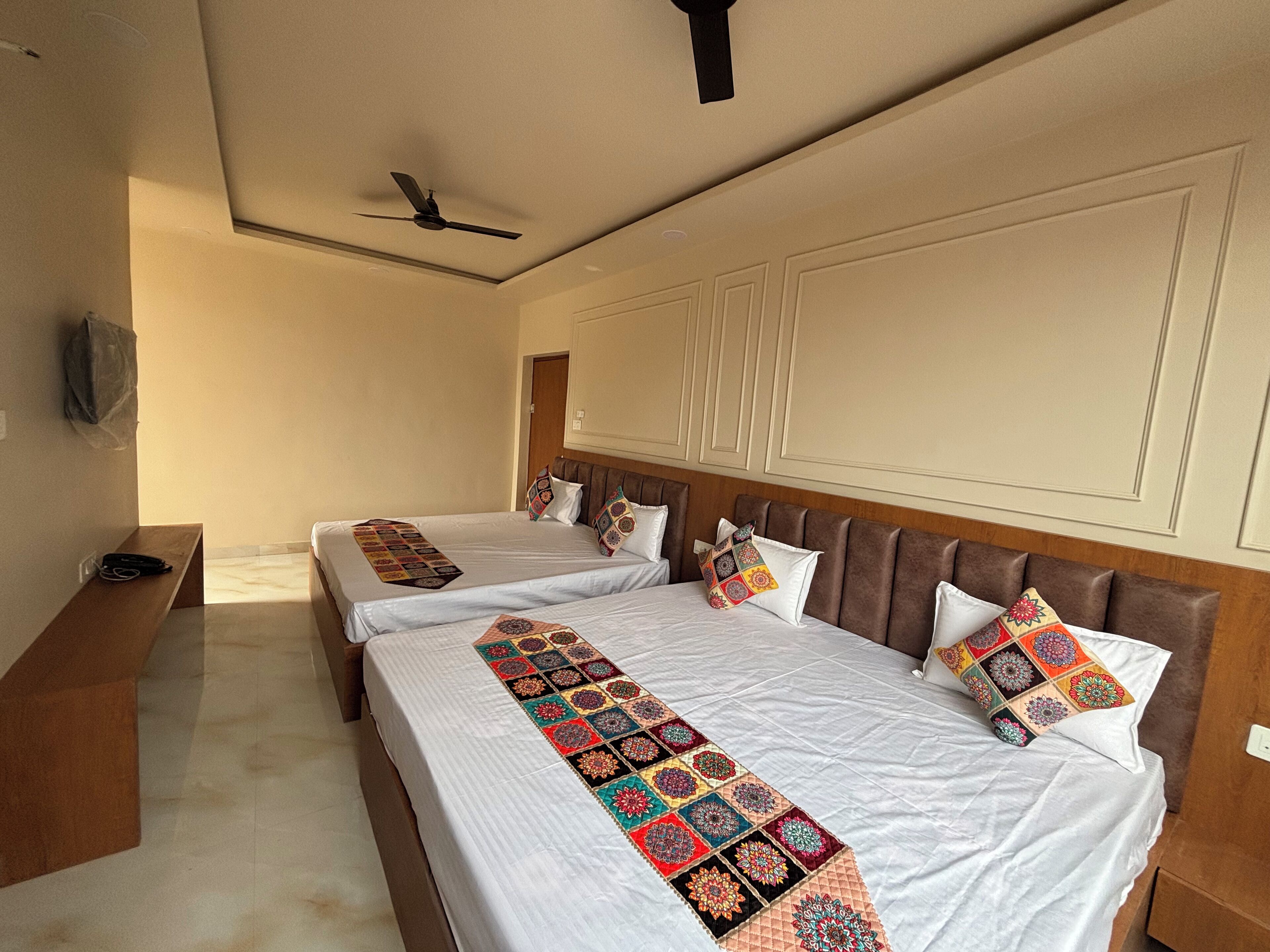A hotel room with two beds, a wooden headboard, a ceiling fan, and a bench.