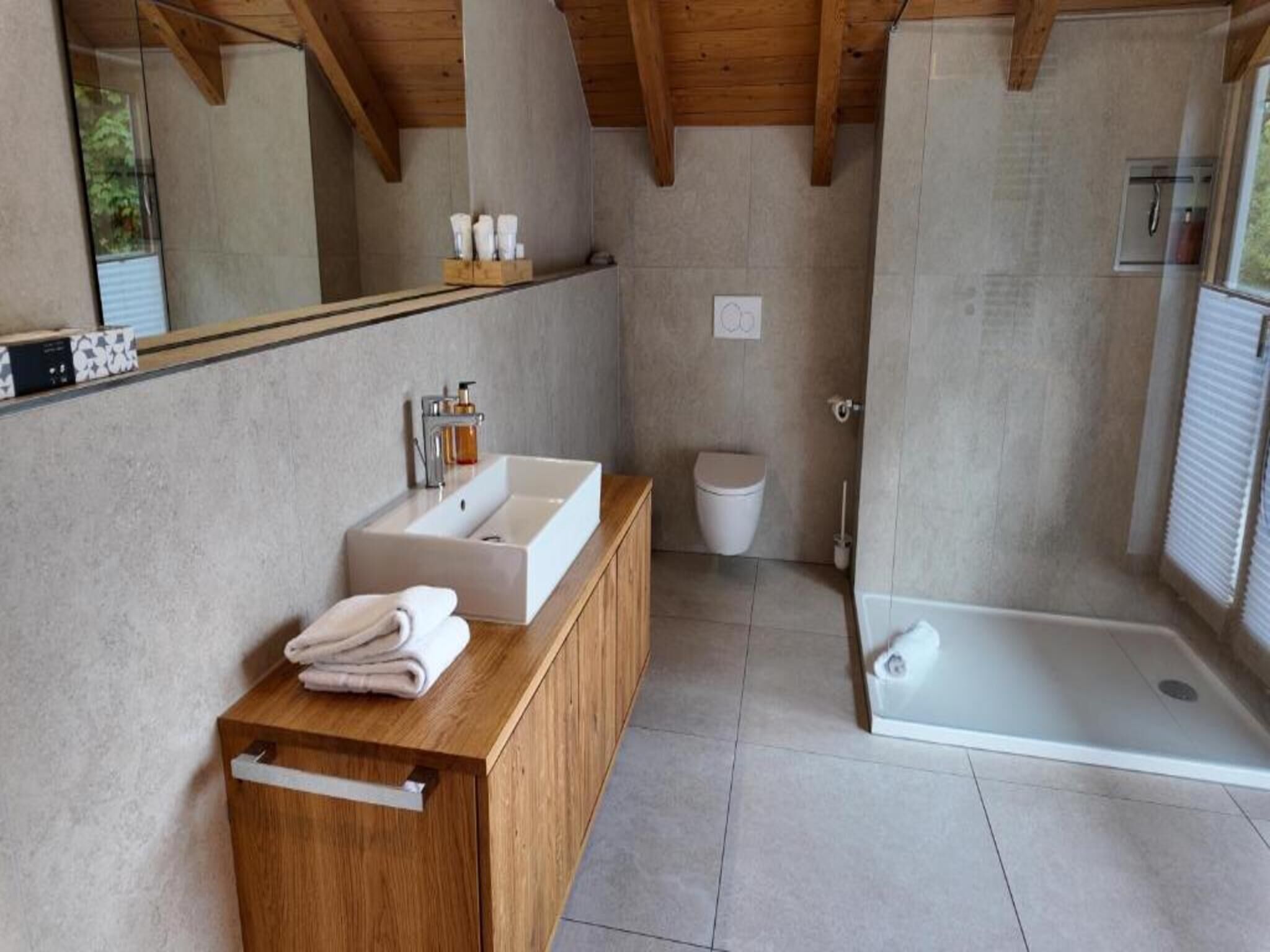 A modern bathroom with a wooden vanity, a large mirror, a white sink, and a glass-enclosed shower.