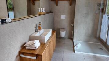 A modern bathroom with a wooden vanity, a large mirror, a white sink, and a glass-enclosed shower.