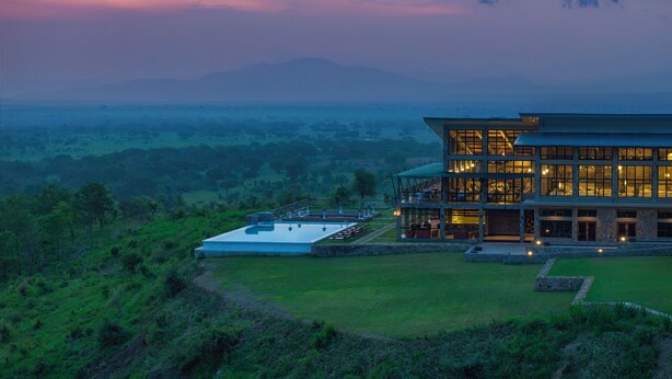 A modern building with a flat roof and large windows, surrounded by lush greenery and distant mountains. - WELLWORTH MIKUMI WILDLIFE LODGE (Morogoro)