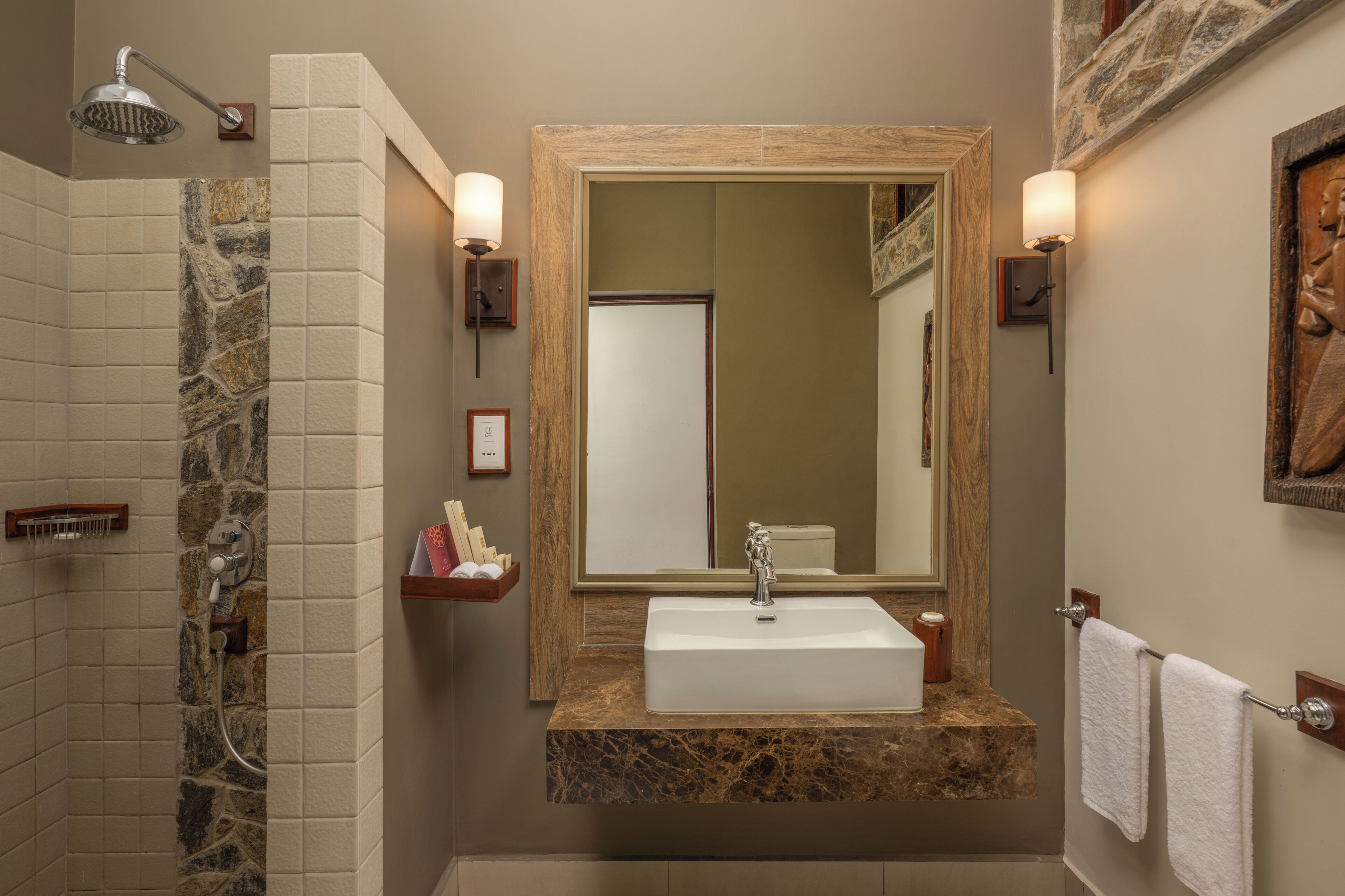 A bathroom with a stone shower, a marble countertop sink, and a large mirror.