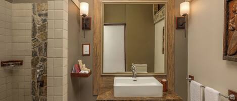 A bathroom with a stone shower, a marble countertop sink, and a large mirror.
