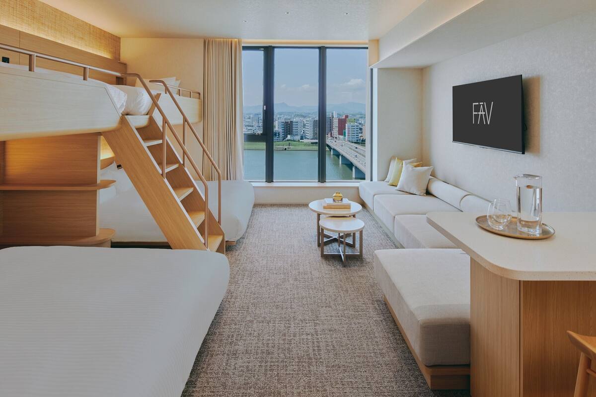 A hotel room with a bunk bed, a sofa, a small table with a tray, and a TV on the wall.