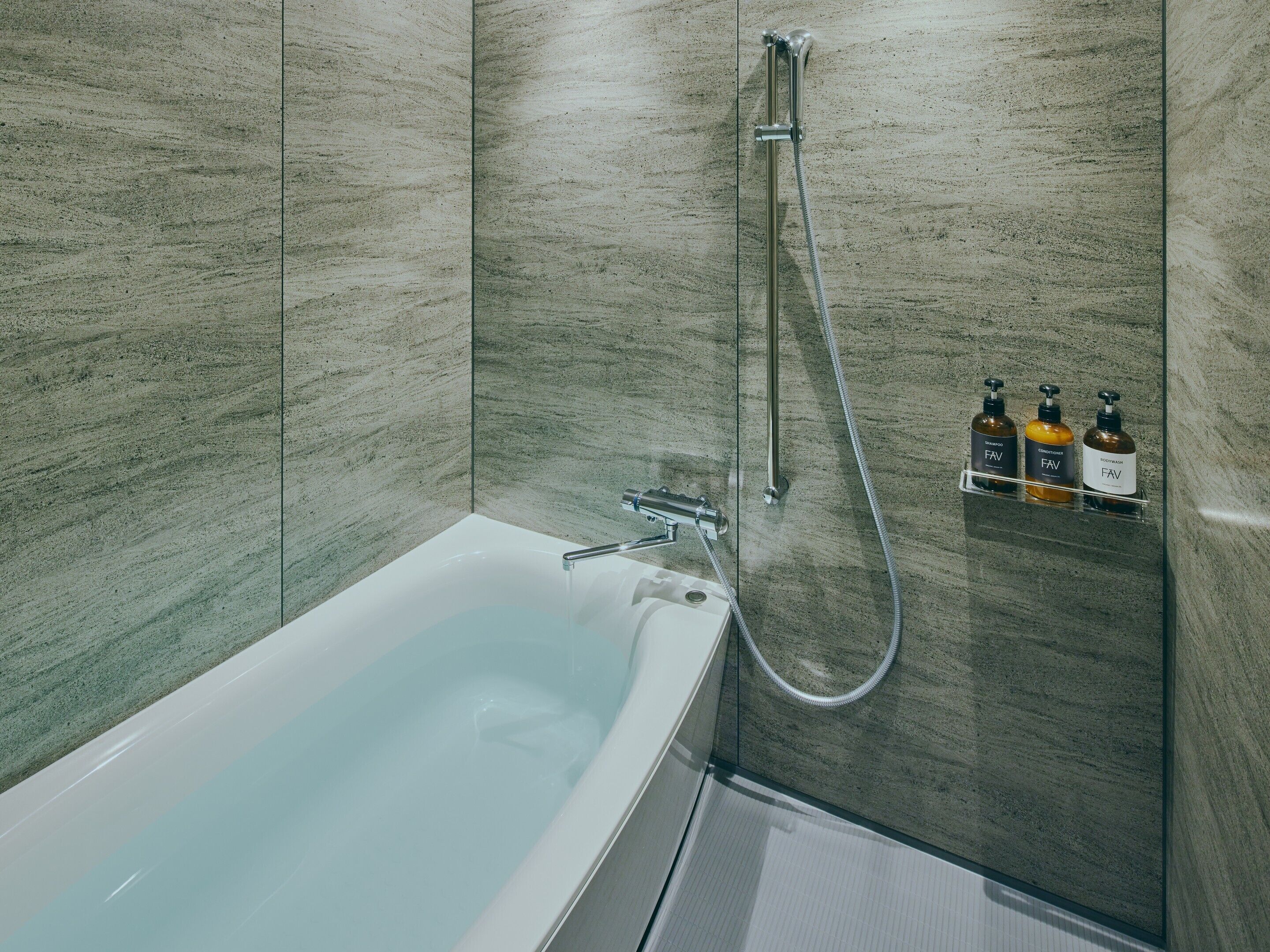 A modern bathroom with a bathtub, shower, and three bottles of toiletries on a shelf.