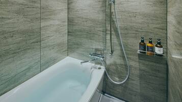 A modern bathroom with a bathtub, shower, and three bottles of toiletries on a shelf.