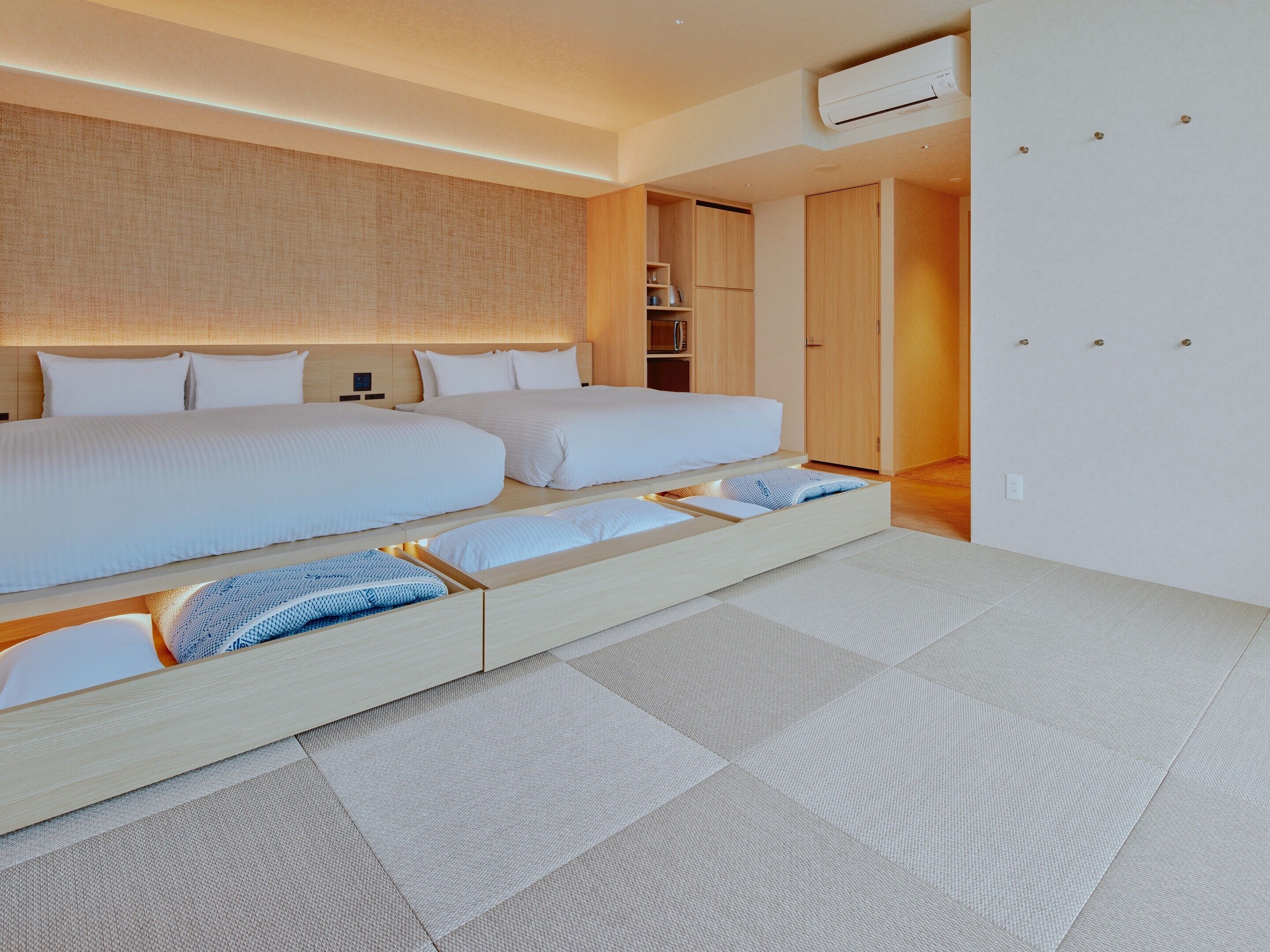 A modern hotel room with a large bed, built-in storage, and a visible air conditioning unit.