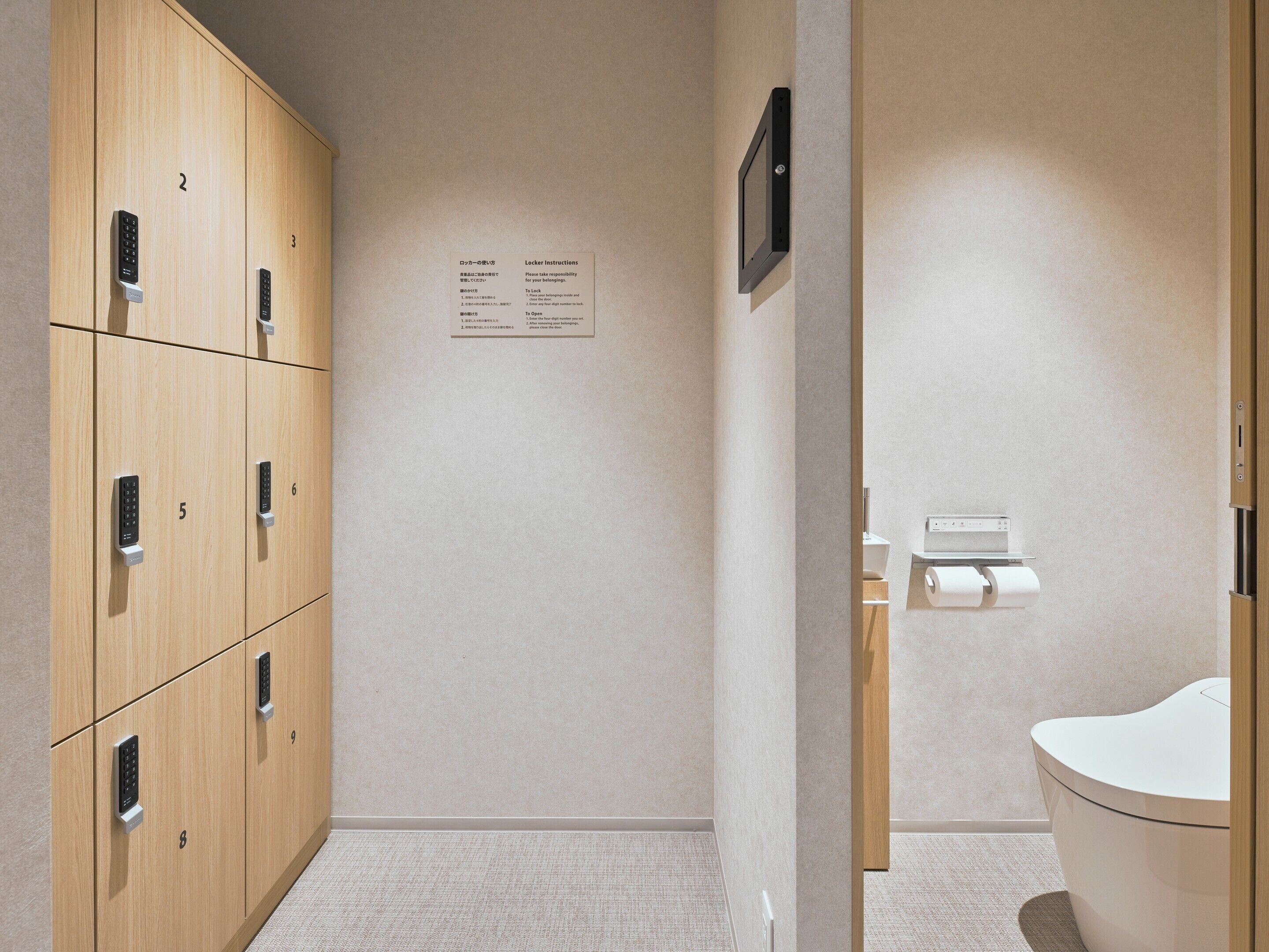 A hotel bathroom with wooden lockers, a toilet, and a paper towel dispenser.