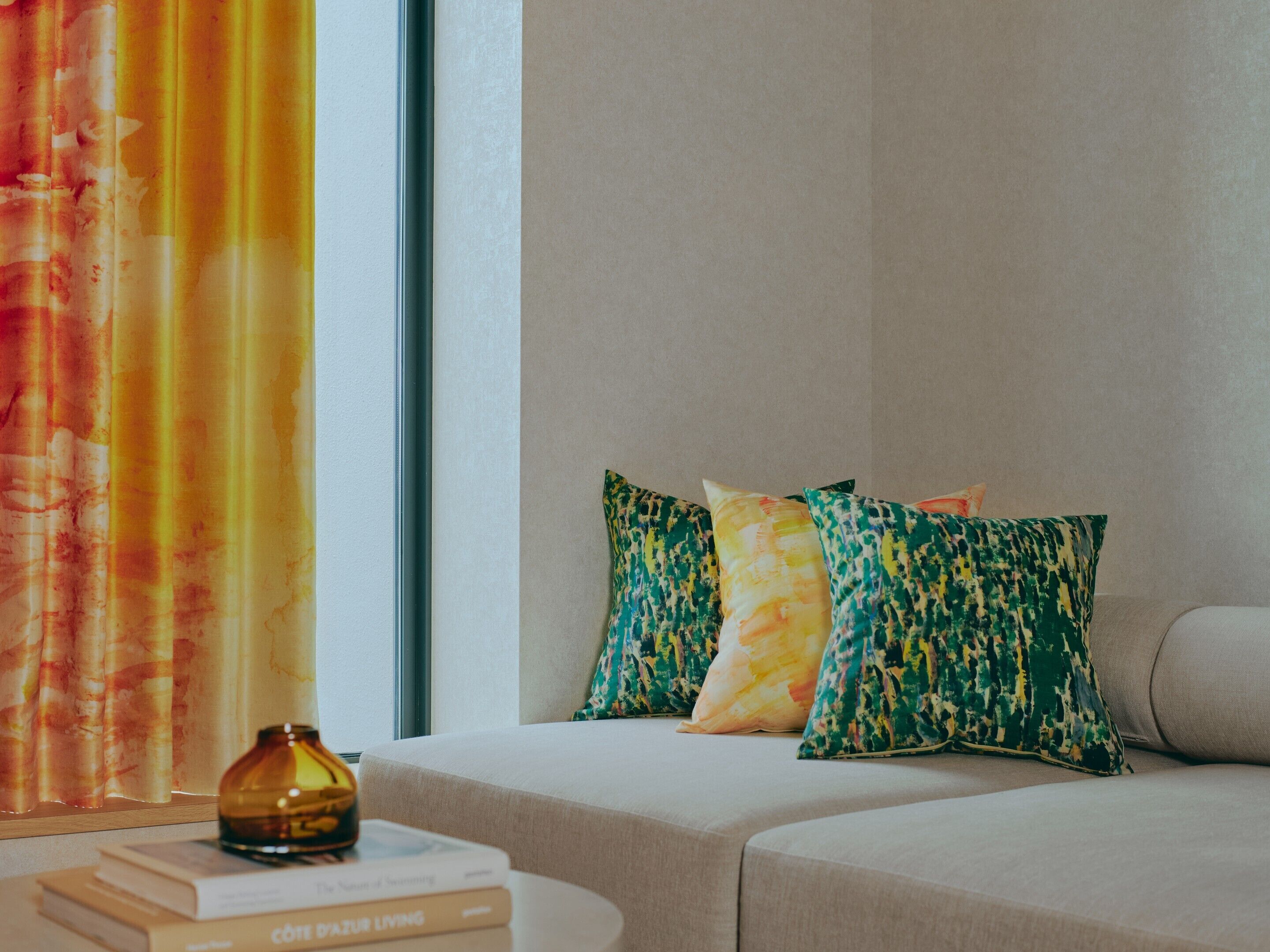 A room with a sofa, a window with curtains, and a small table with books and a vase.