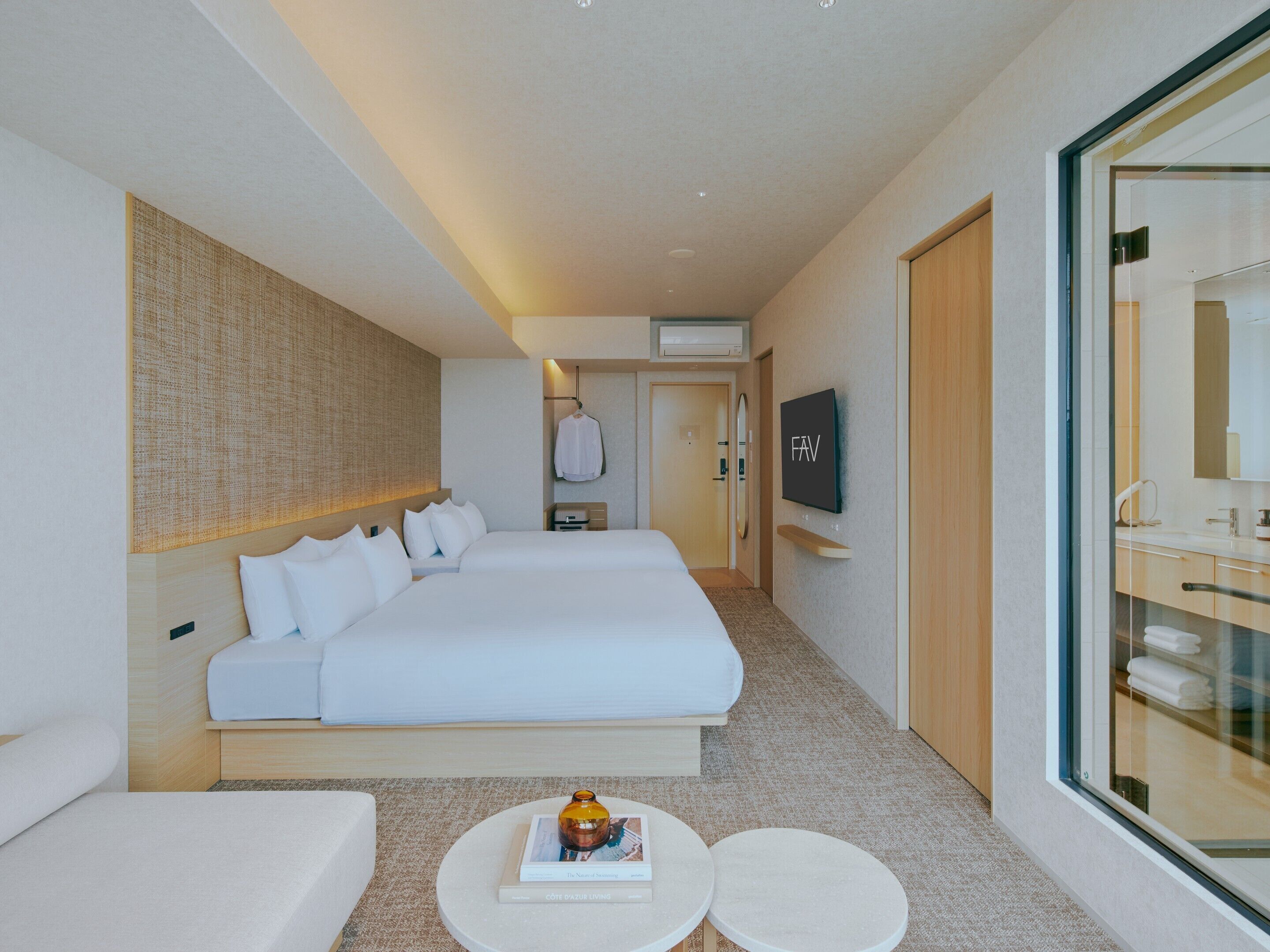 Habitación de hotel con una cama grande, televisión, minibar y baño con paredes de vidrio.