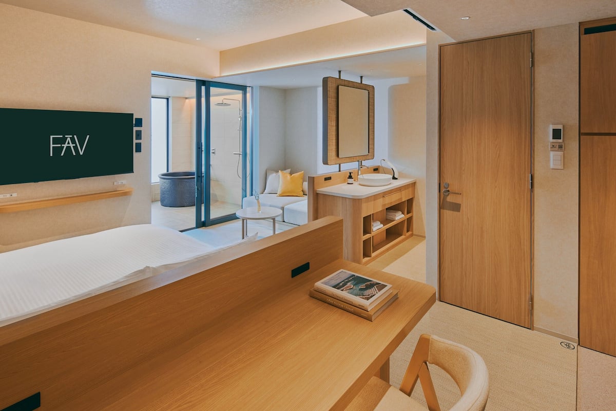A modern hotel room with a wooden vanity, a large mirror, a sofa, and a separate seating area with a chair.