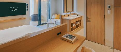 A modern hotel room with a wooden vanity, a large mirror, a sofa, and a separate seating area with a chair.