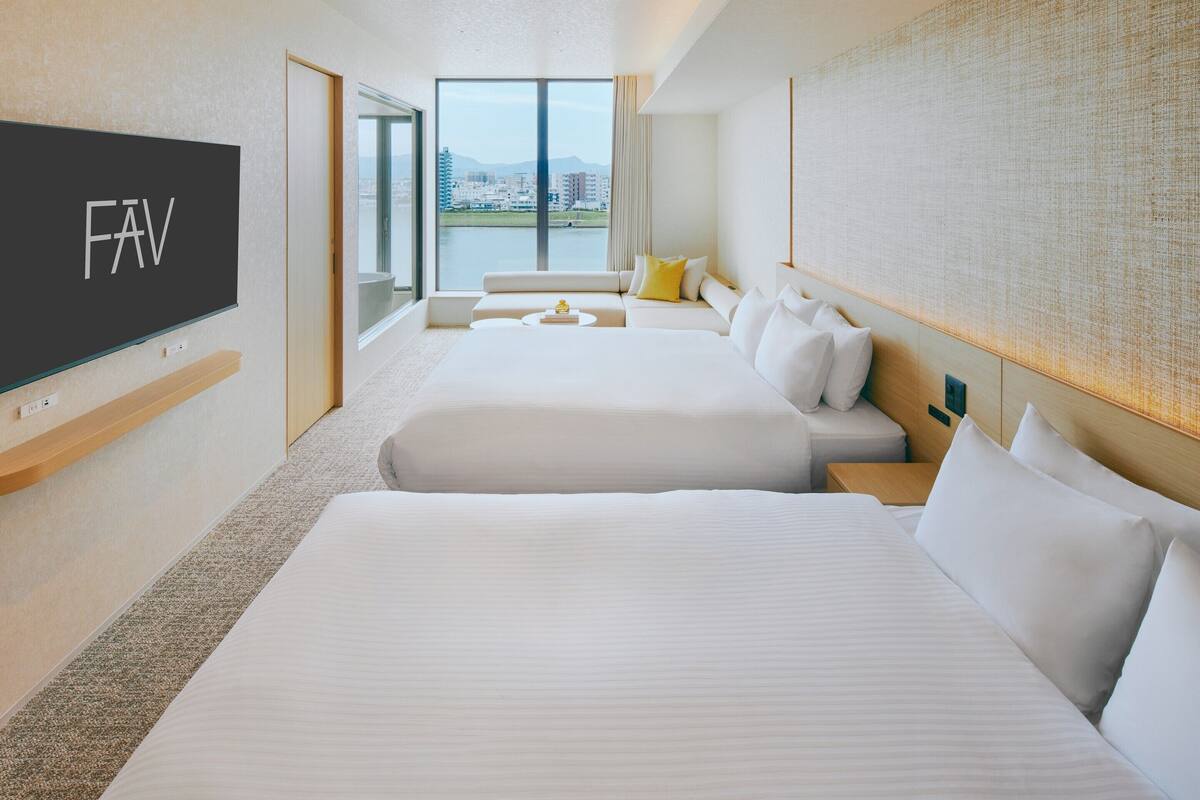 A hotel room with two beds, a TV, a sofa, and a large window with a view.