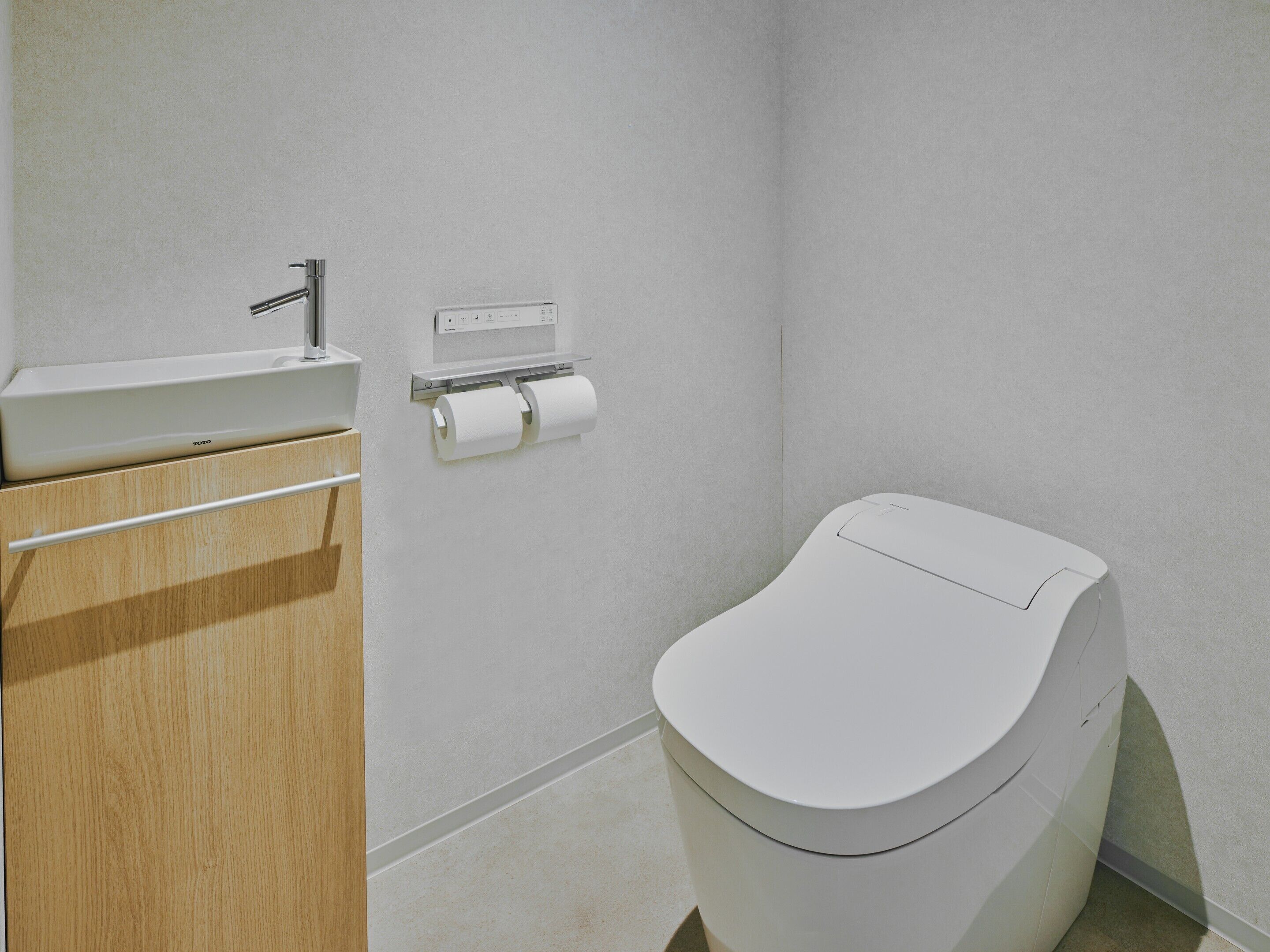 Uma casa de banho moderna com sanita, lavatório e dispensador de papel.