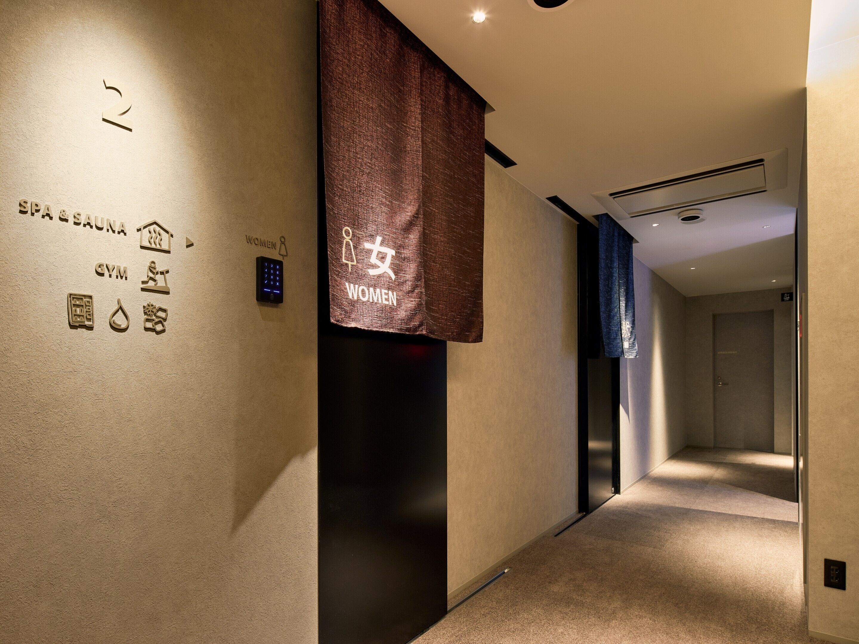 A hallway with a spa and sauna sign, a women-only sign, and a digital elevator control panel.