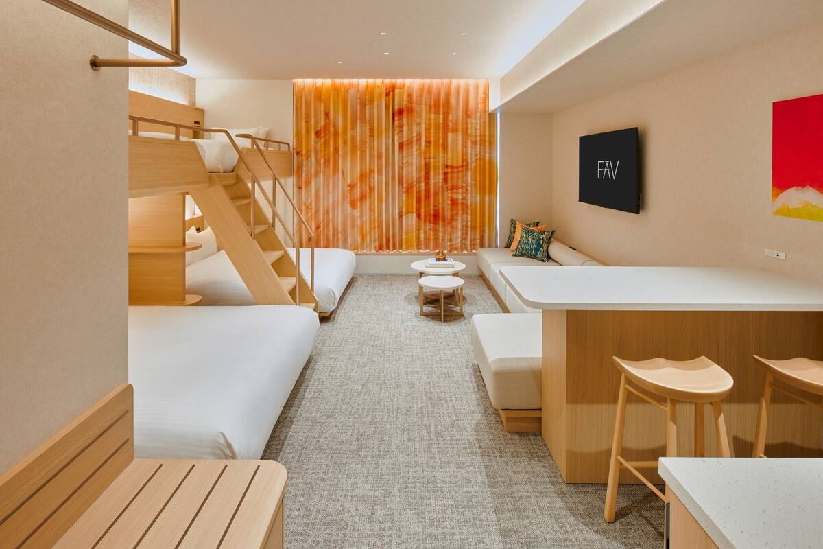 A modern hotel room with a bunk bed, a sofa, a small round table, and a bar area.