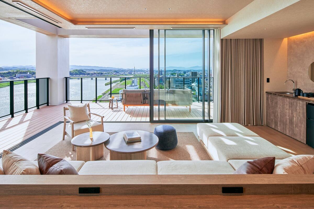 A modern living room with a sofa, coffee table, and a view of a cityscape through large windows.