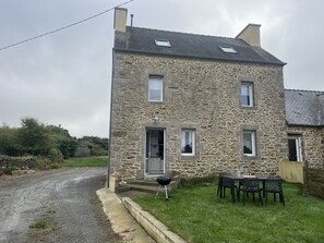 A stone house with a paved driveway, a barbecue grill, and a table with chairs outside. - House for 7 with Garden – Very Quiet Neighborhood (Plouguerneau)
