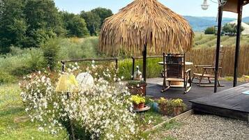 A thatched-roof gazebo, outdoor seating, and a garden with flowers and plants.