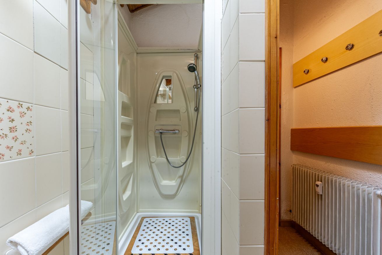 A shower stall with a glass door, a wooden bench, and a tiled wall with a floral pattern.