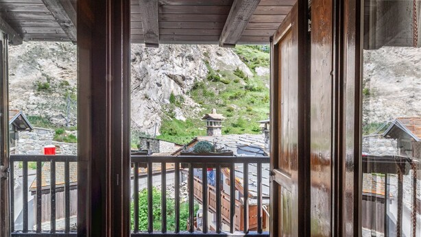 A wooden balcony with a view of a mountain and traditional buildings. - 🏠 PROPERTY DESCRIPTIONWelcome to Casa Alpina, in the heart of La Thuile, Valle d’Aosta. A typical mountain apartment, cozy and comfortable, immersed in the tranquility of an alpine village. Ideal for those seeking relaxation, nature, and ski slopes  (La Thuile)