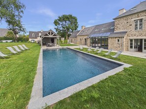 A rectangular swimming pool with lounge chairs and a covered patio area. - House for 12 with large garden and swimming pool (Tréméreuc)