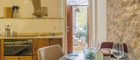 A dining area with a glass table set for two, a stone wall, and a view of the outside.
