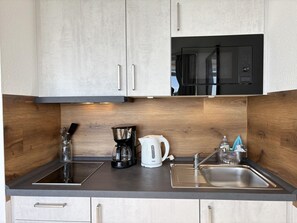 A modern kitchen with a stainless steel sink, a coffee maker, a kettle, and a microwave. - Strandhotel - 19 "Sardine tin" - More sea views from the "sardine tin"! (Dahme)