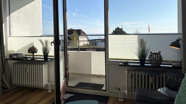 Ein Zimmer mit einer Glastür zu einem Balkon, einem Heizkörper, einem kleinen Tisch mit Lampe und einem Sofa.