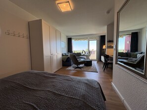 Une chambre à coucher comprenant un lit, un bureau, une chaise, une armoire et un balcon avec vue.