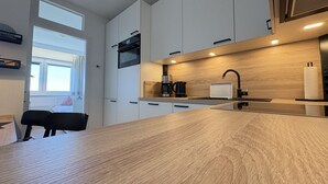 A modern kitchen with white cabinets, a wooden countertop, a coffee maker, and a window with curtains. - Berolina 801 - Meerestraum - "Sea dream"... exclusive vacation apartment in the house (Dahme)