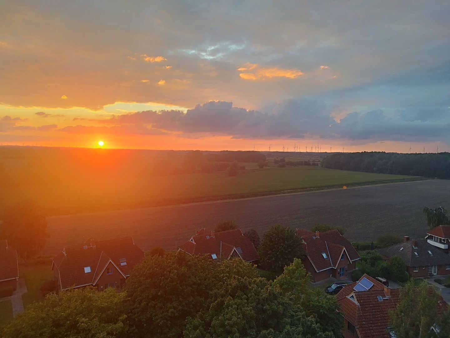 A sunset over a rural landscape with wind turbines in the distance.