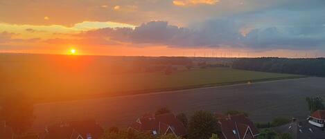 A sunset over a rural landscape with wind turbines in the distance.