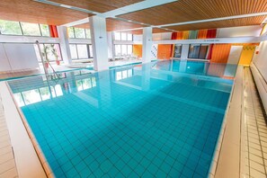 Une piscine intérieure à l’eau claire, aux murs carrelés et à l’intérieur baigné de lumière naturelle.