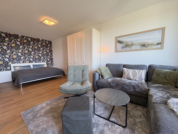 Une chambre à coucher avec un lit, une chaise, un canapé, une petite table et un tableau accroché au mur.