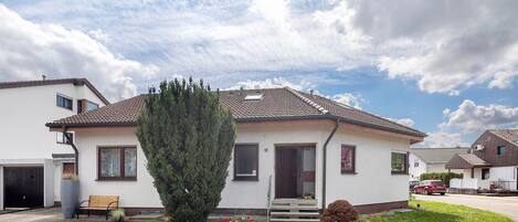 Een gelijkvloers huis met een veranda, een garage en een verzorgde tuin met bloemen en een boom.