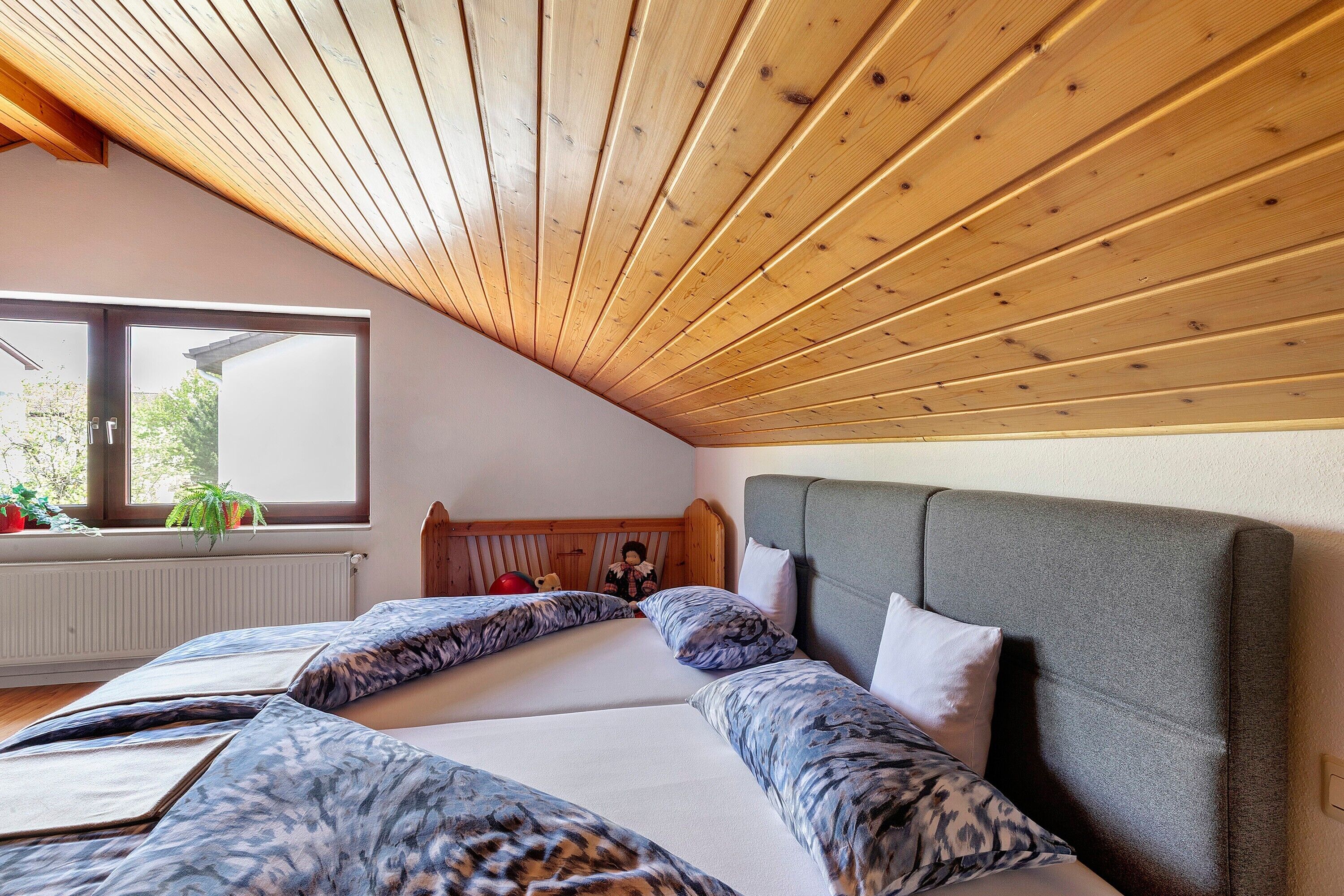 Een slaapkamer met een schuine kap, een groot raam en een bed met beddengoed met een patroon.