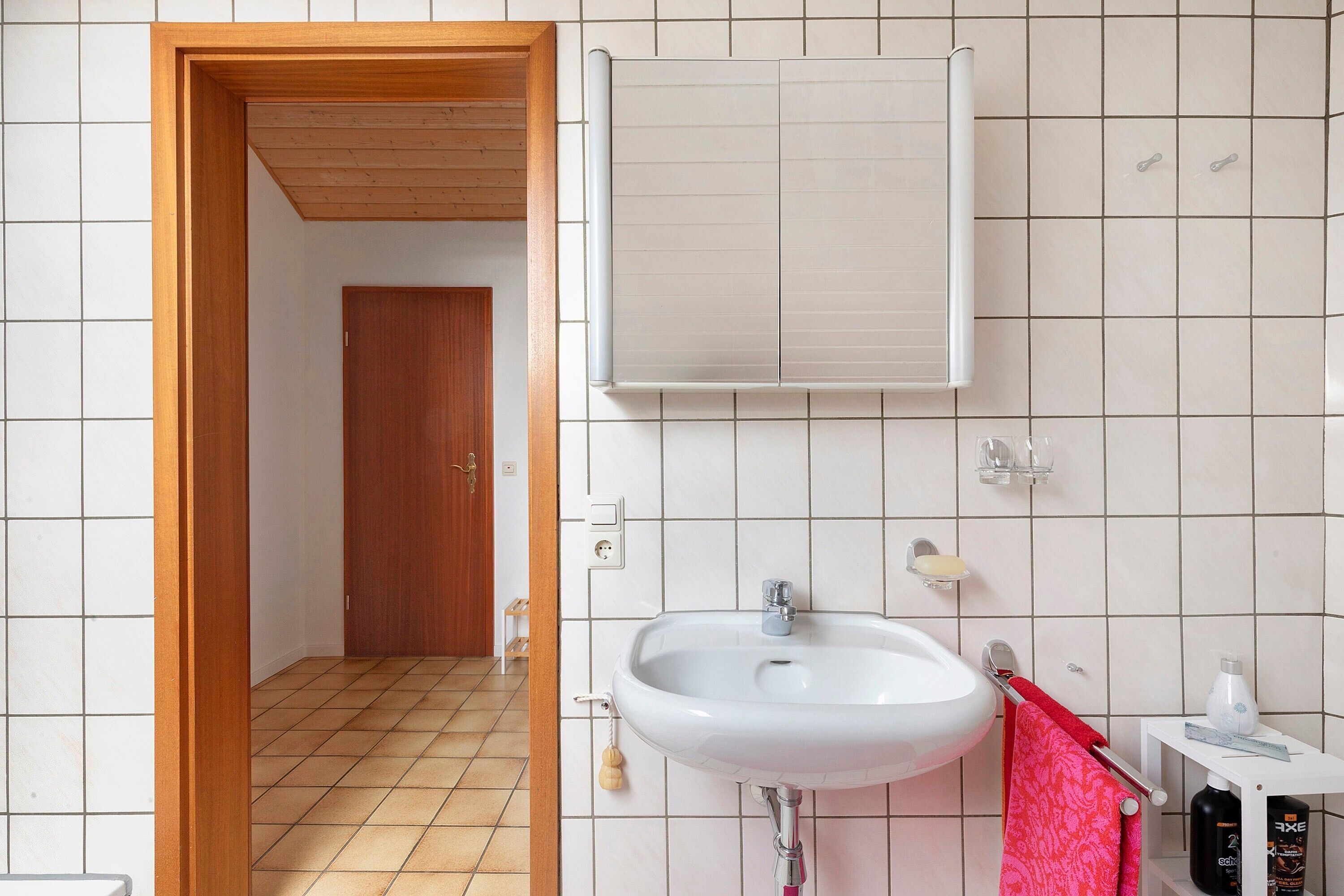 Une salle de bain avec un lavabo blanc, une porte en bois et un sol carrelé.