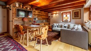 Een rustiek interieur met een houten eettafel, stoelen, een bank en een televisie bevestigd aan een houten wand.