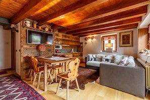 Un intérieur rustique avec une table à manger en bois, des chaises, un canapé et un téléviseur fixé à un mur en bois.