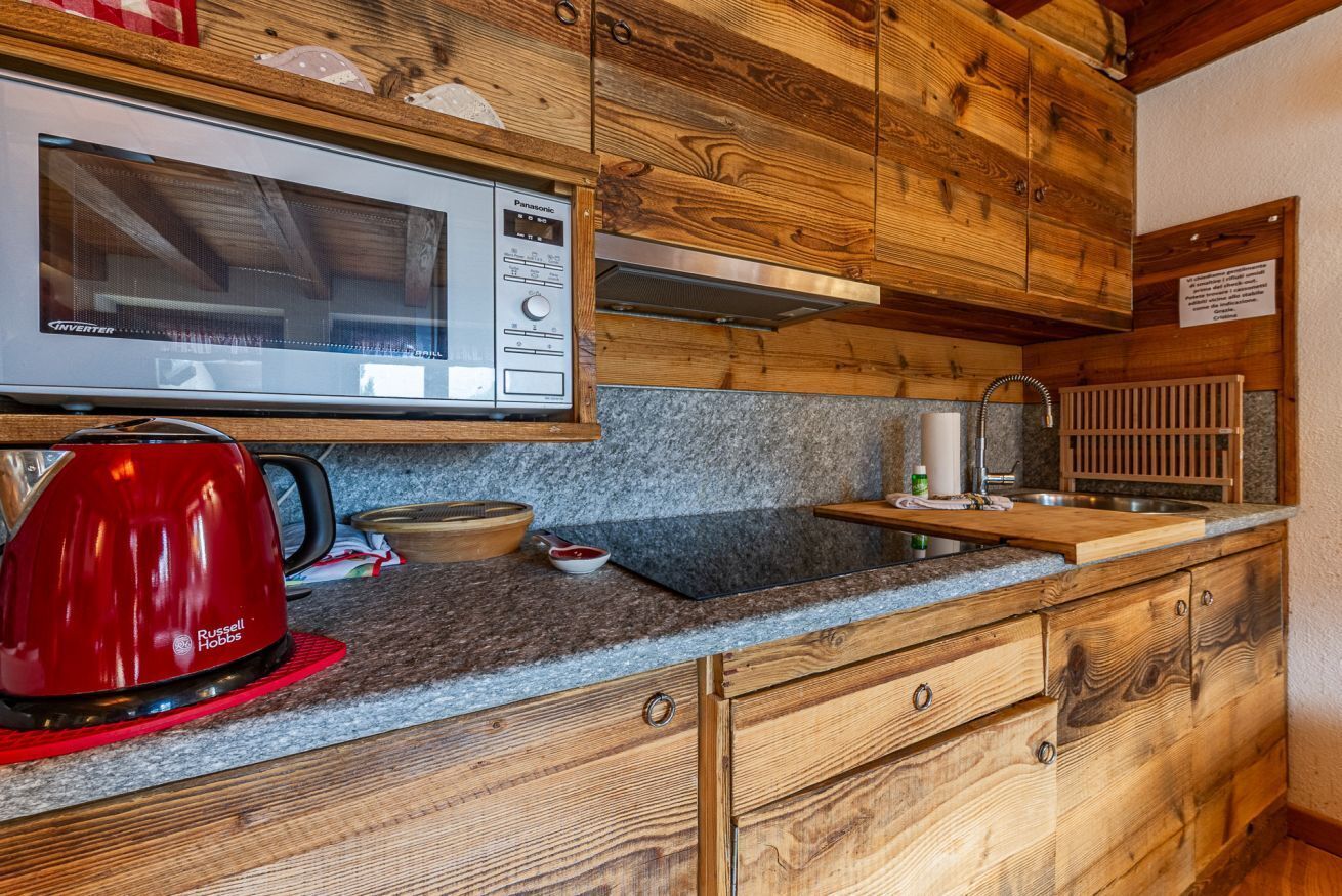 A kitchen with wooden cabinets, a microwave, a kettle, and granite countertops.