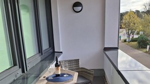 A balcony with a table set for two, wicker chairs, a bottle of wine, and a glass. - Vacation apartment Meer-Zeit in Lubmin (Lubmin)