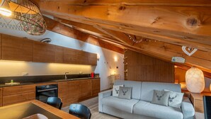 A cozy cabin interior with a wooden ceiling, a sofa with decorative pillows, a dining area with a table, and a kitchen with wooden cabinets. - APT JARDIN DES ALPES - Let yourself be enchanted by the magic of the mountains (La Thuile)