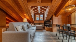 A cozy loft-style room with a wooden ceiling, a sofa, a TV, and a dining area. - APT JARDIN DES ALPES - Let yourself be enchanted by the magic of the mountains (La Thuile)
