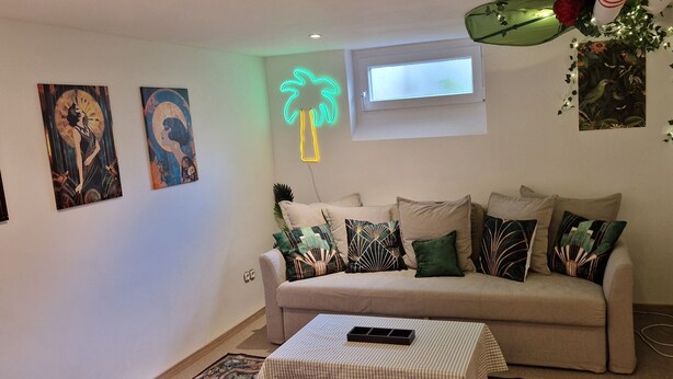 Una sala de estar con un sofá, una mesa de centro y un letrero luminoso con forma de palmera.