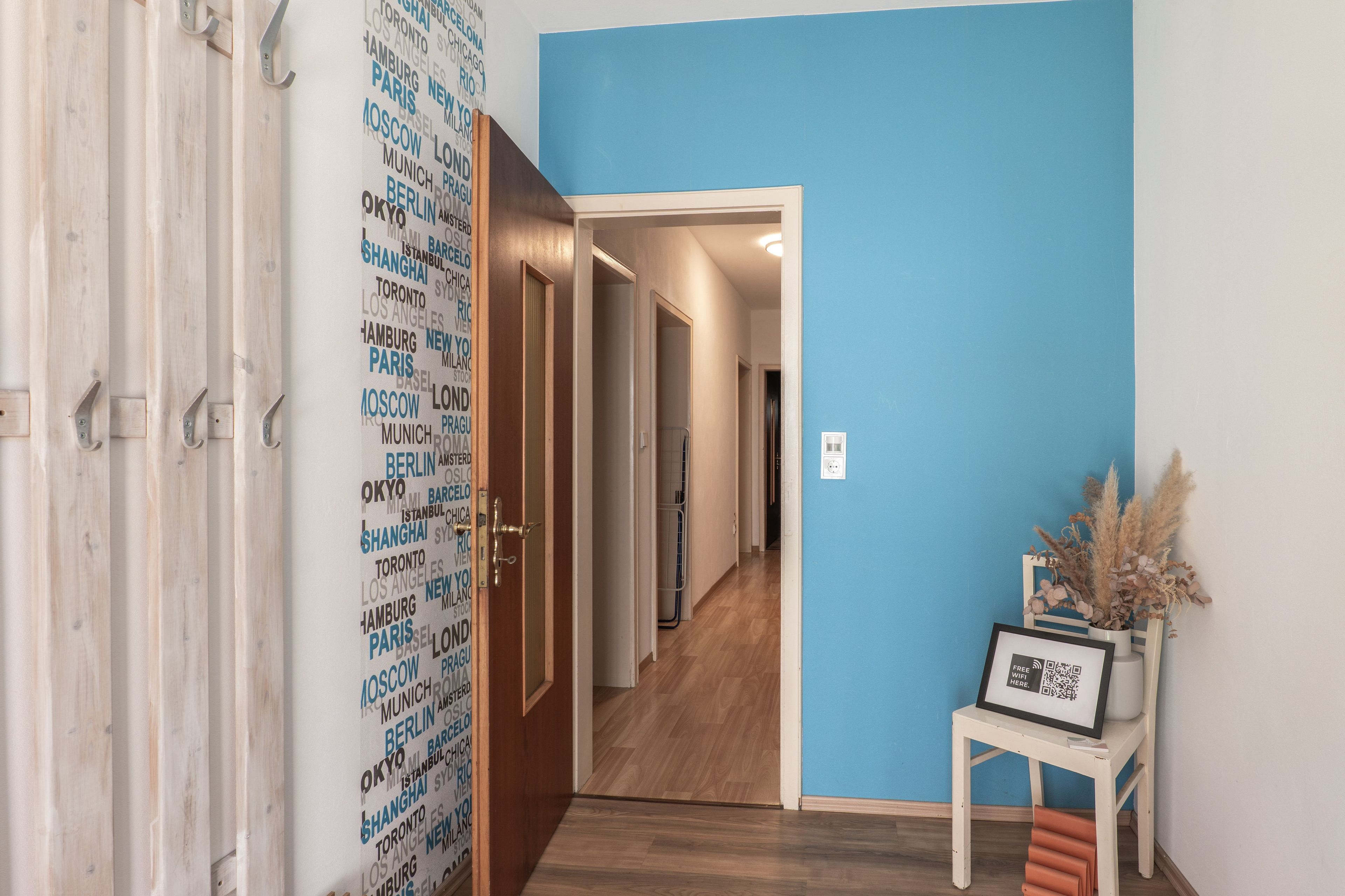 Un pasillo con una pared azul, una puerta de madera con un picaporte metálico y un cuadro enmarcado sobre una pequeña mesa.