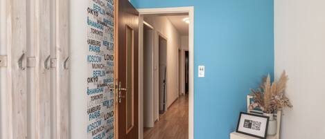 Un pasillo con una pared azul, una puerta de madera con un picaporte metálico y un cuadro enmarcado sobre una pequeña mesa.