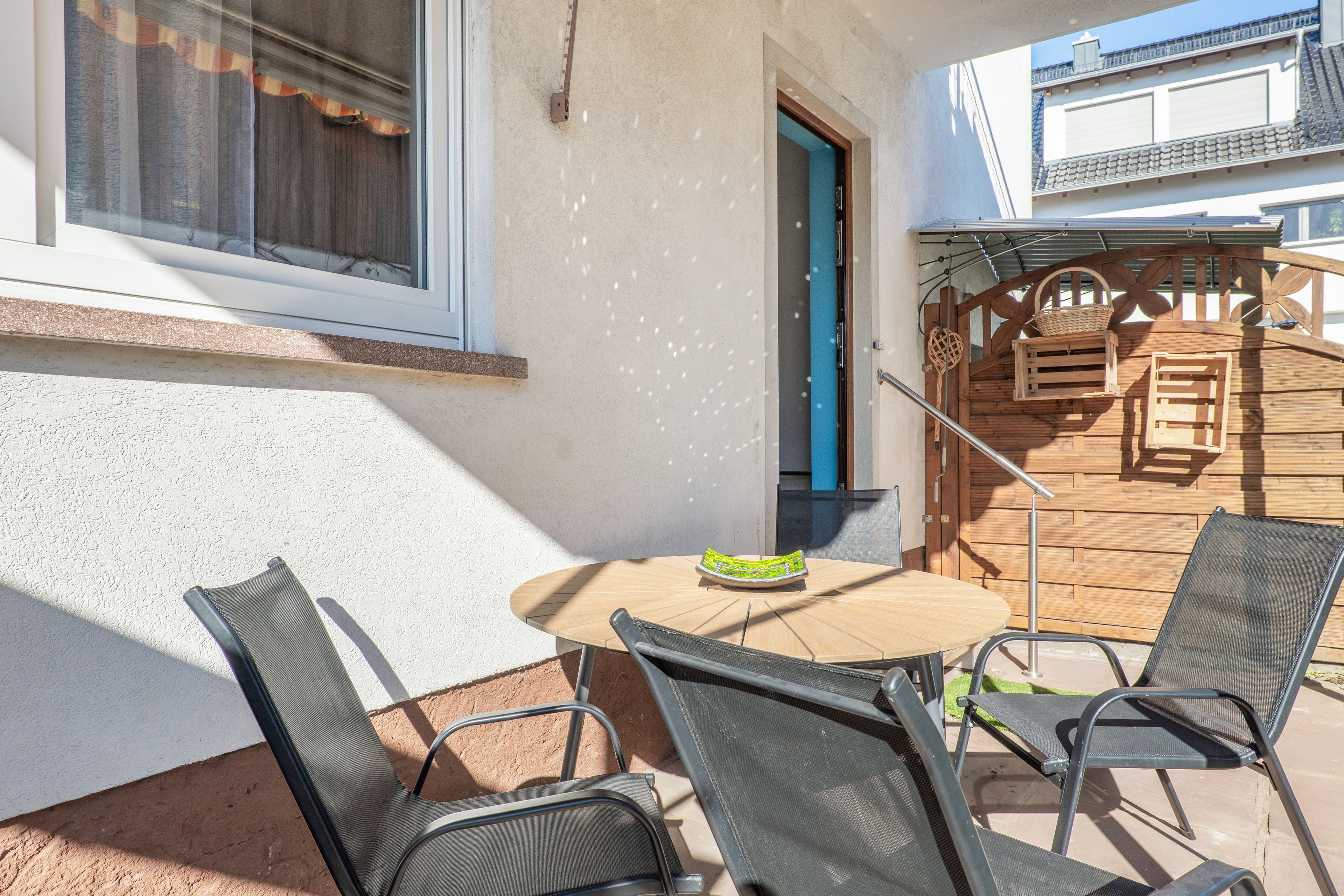 An outdoor patio with a round table and four chairs, a wooden door, and a metal gate leading to a deck.