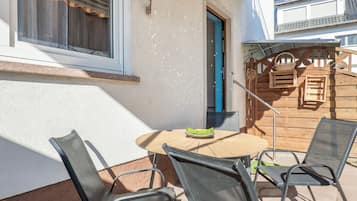 An outdoor patio with a round table and four chairs, a wooden door, and a metal gate leading to a deck.